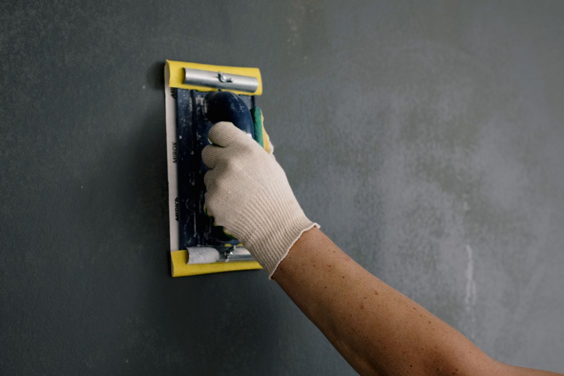 Vakman met witte handschoenen die met een schraper een muur controleert en bijwerkt