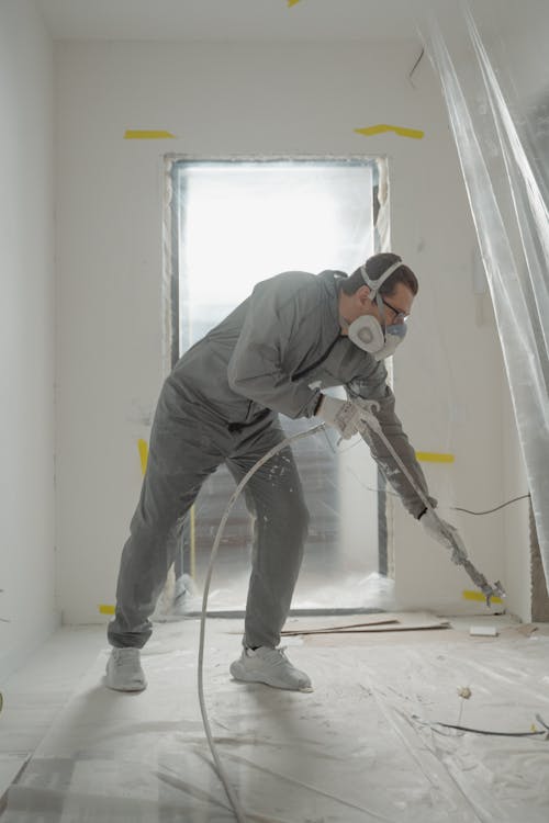Vakman in werkkleding die met airless spuit latex aanbrengt tijdens een binnenverbouwing