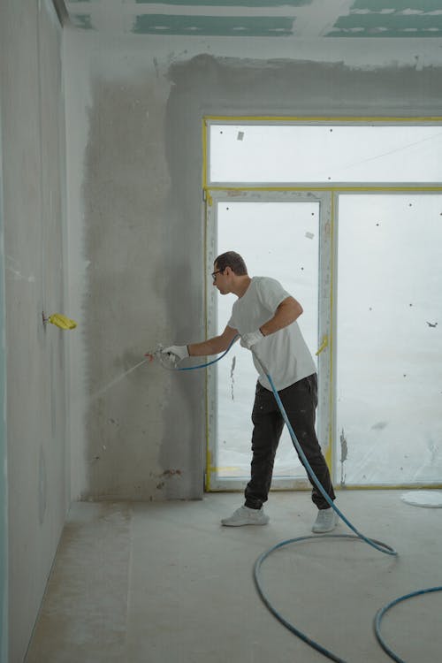 Vakman die met airless spuitpistool latex aanbrengt op een binnenwand tijdens renovatie