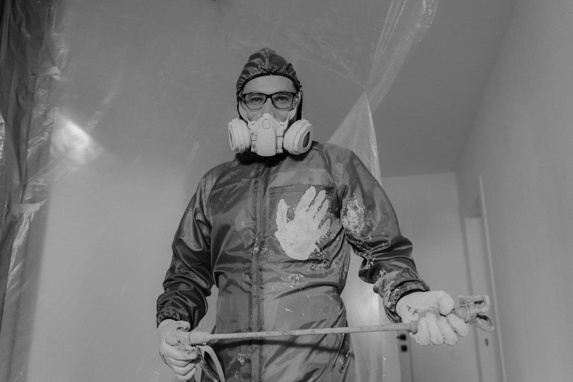 Vakman die met airless spuit het plafond bewerkt in een lege woonkamer tijdens verbouwing