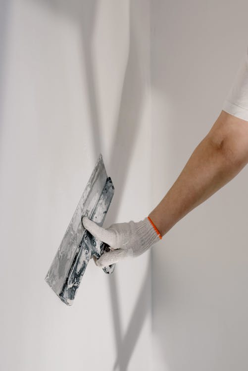 Hand van stukadoor in handschoen die met spatel een dunne afwerklaag aanbrengt op een muur