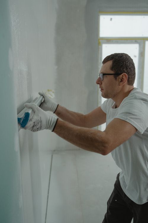 Stukadoor die dunpleister aanbrengt op een muur, gereedschap zichtbaar op de achtergrond