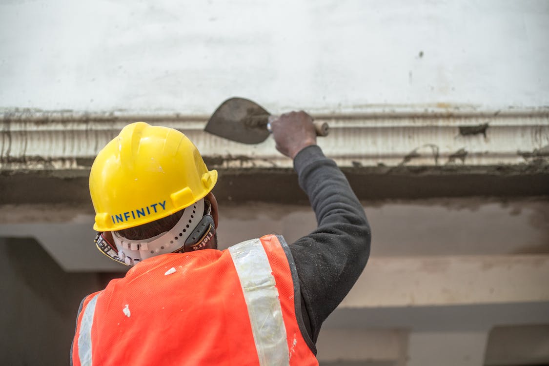 Stukadoor in veiligheidshelm en masker die met troffel pleisterwerk aanbrengt bij een renovatie