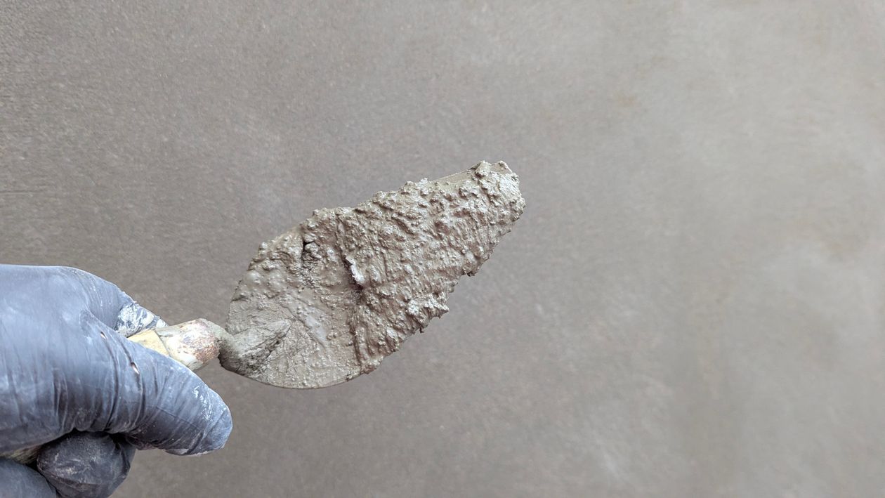 Vakman met handschoen die een pleisterspaan tegen een muur houdt, klaar om sierpleister aan te brengen in Tilburg