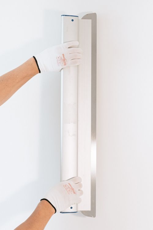 Vakman met handschoenen die met een spaan een muur gladstrijkt bij het aanbrengen van sierpleister in een woning in Tilburg