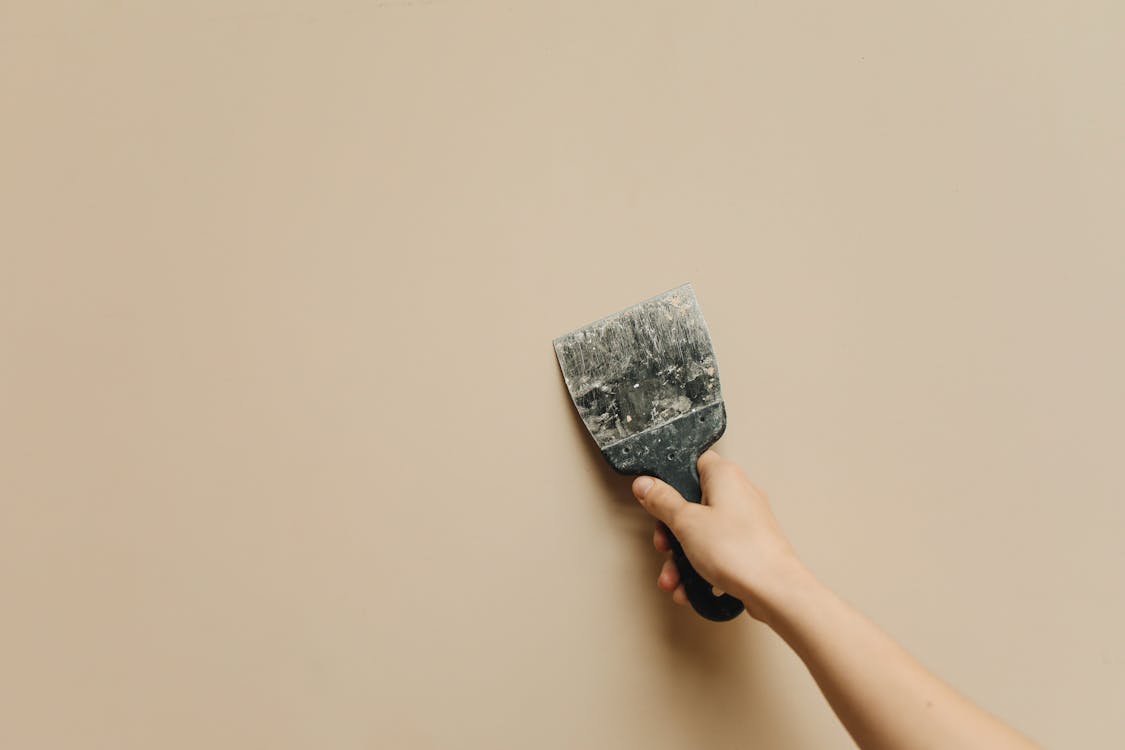 Hand met metselspaan die pleisterlaag egaal verdeelt over een wand