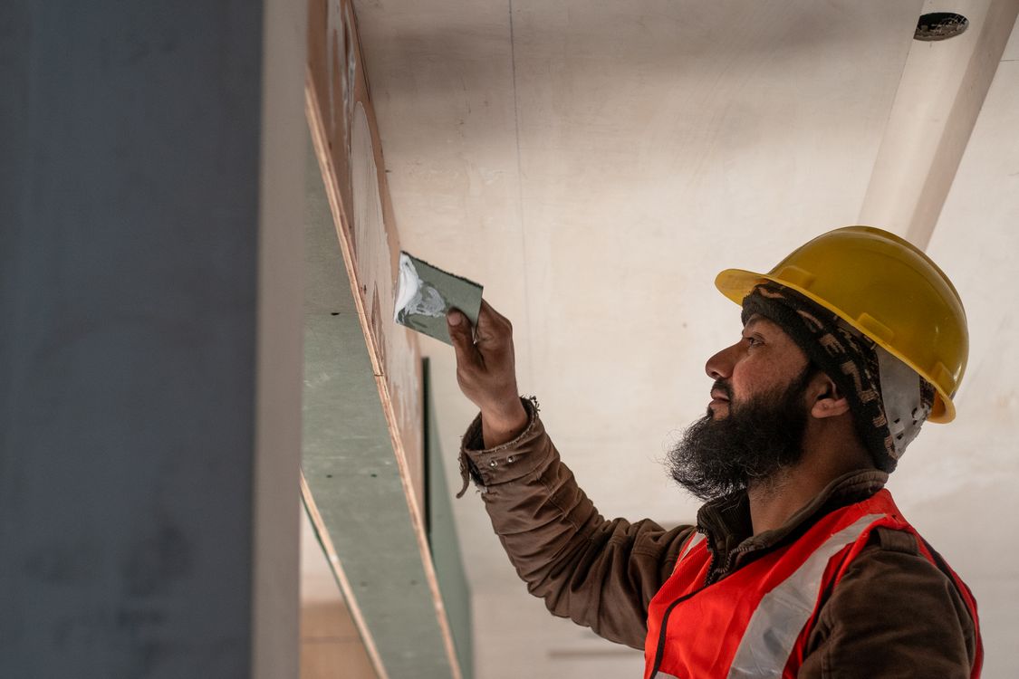 Stukadoor die pleisterwerk aanbrengt op een plafond in een woning in Tilburg, fysiek zwaarder werk dan een wand