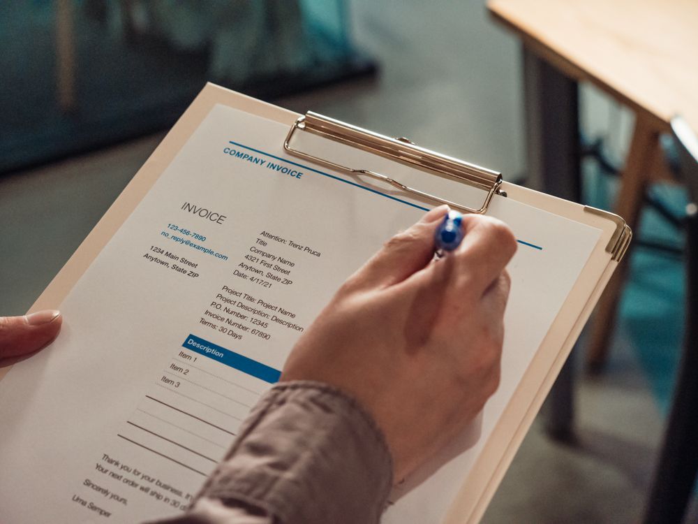 Hand met pen bij een factuur op een klembord als illustratie van kosten