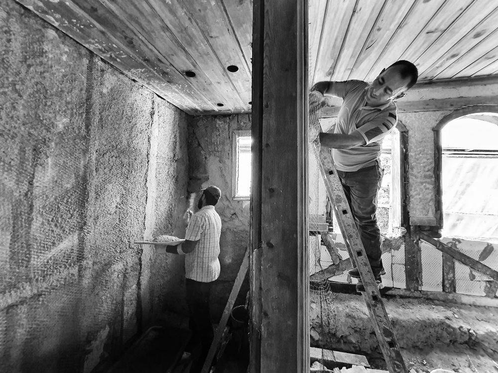 Twee vaklieden renoveren een kamer, één op ladder bezig met pleisterwerk