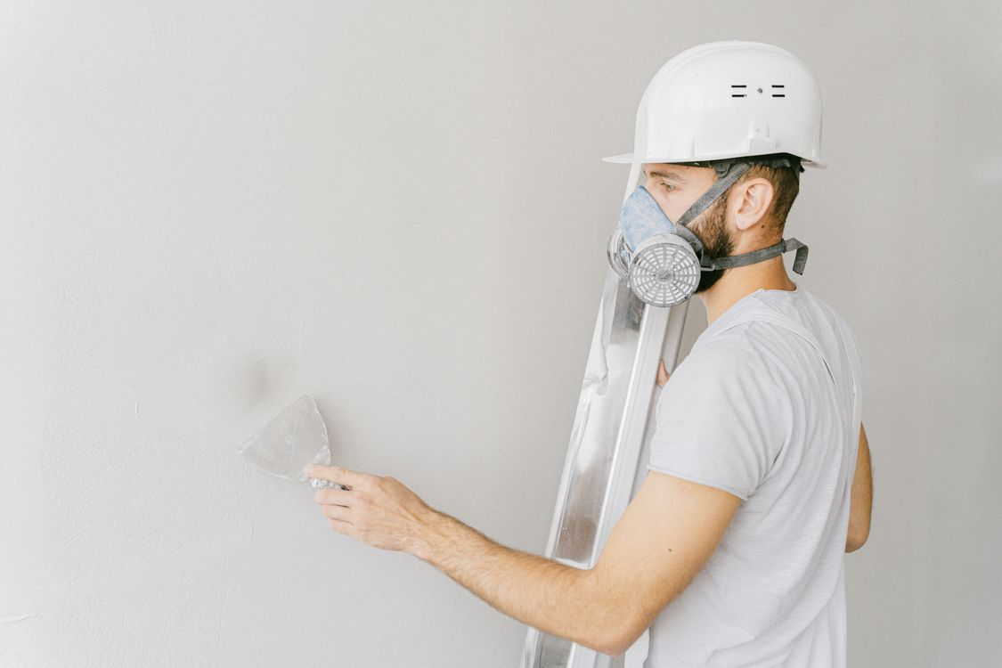 Bouwvakker met gasmasker en helm die pleister aanbrengt op een binnenmuur