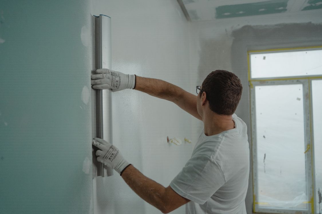 Man met rei en handschoenen die een binnenmuur controleert bij renovatie